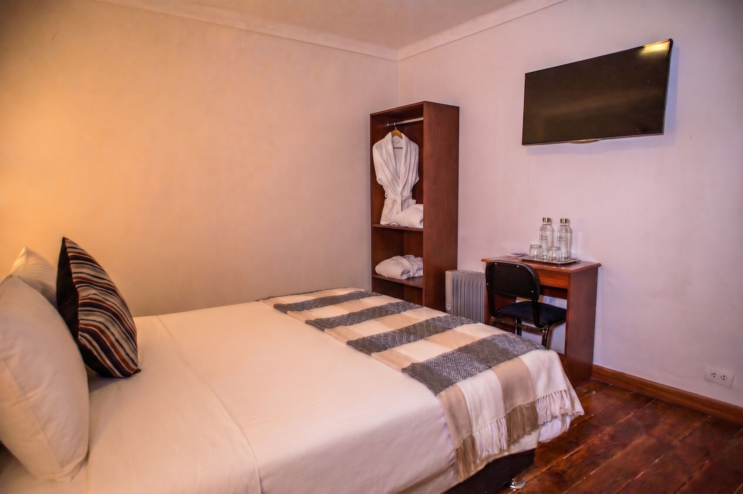 Habitación de hotel con cama, escritorio, silla, bata y televisor de pantalla plana.