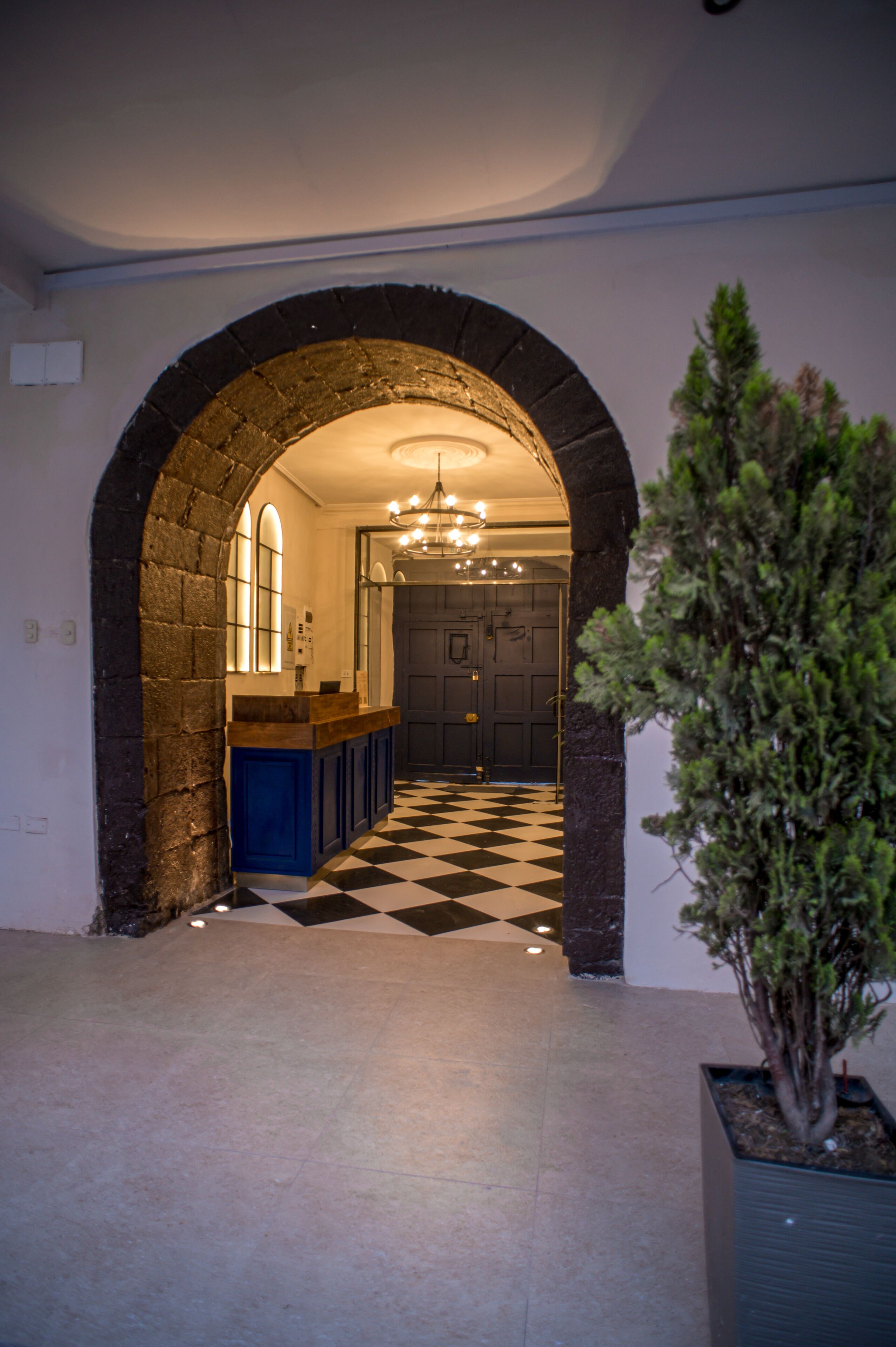 Un arco de entrada conduce a un cuarto con piso a cuadros, una barra de madera y una planta en maceta.
