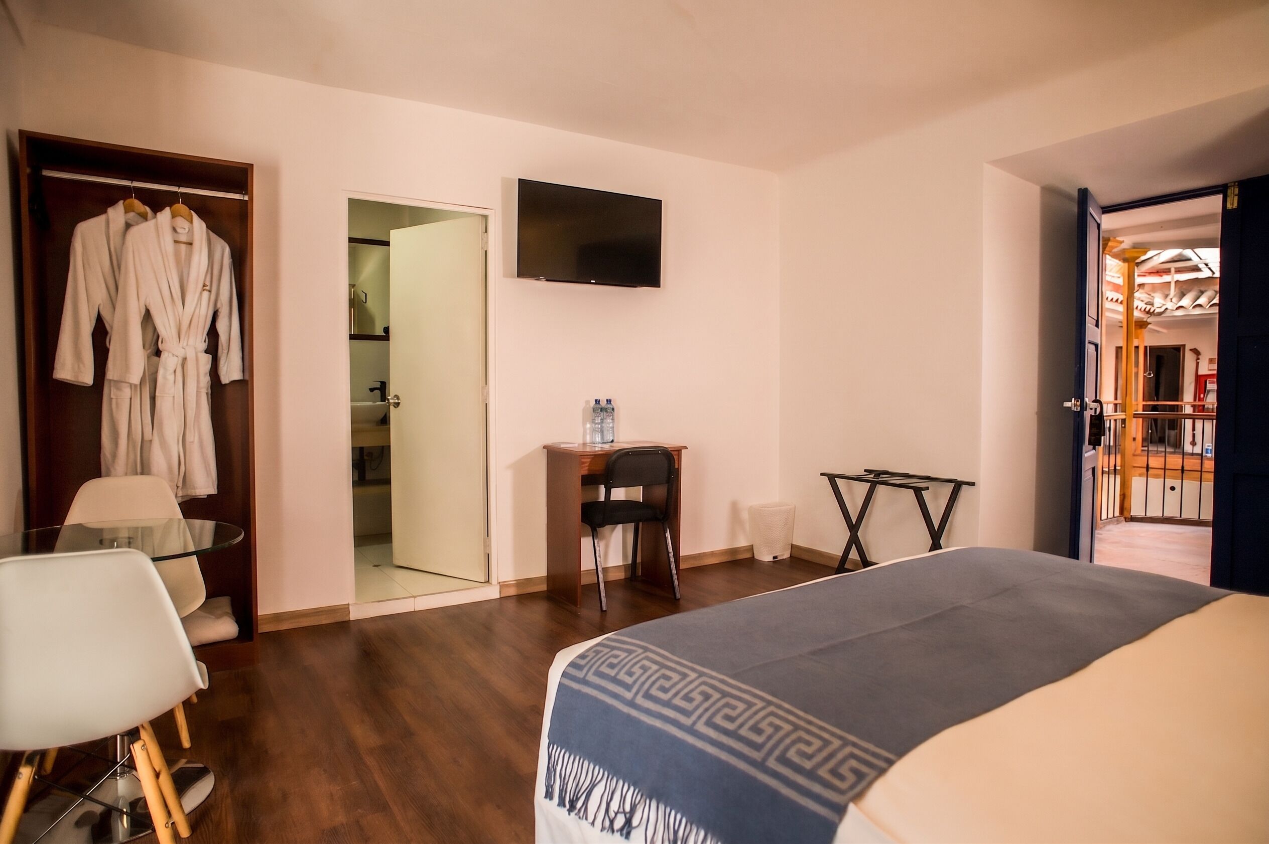 Habitación de hotel con cama, escritorio con silla, televisión y armario con batas.