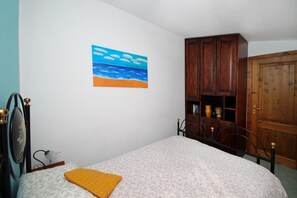 Ein Schlafzimmer mit einem Bett, einem Holzschrank, einem Strandbild und einer kleinen Ablage mit Dekoration.