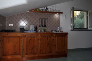 Eine Küche mit Holdekor, einer Arbeitsplatte mit verschiedenen Gegenständen, einem hängenden Küchenutensilienhalter und einem Fenster mit Blick auf Grünflächen.