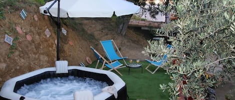 An outdoor hot tub area with a white umbrella, blue lounge chairs, and a small table.