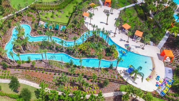Vista aérea de un resort con piscina serpenteante, palmeras y zonas de descanso.