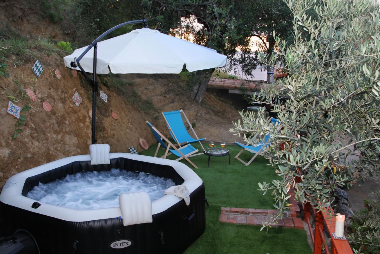 Un área de hidromasaje al aire libre con una sombrilla blanca, sillones reclinables azules y una pequeña mesa.