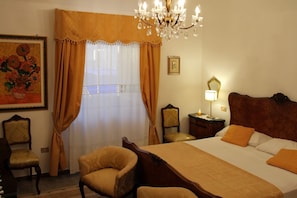 Une chambre d’hôtel avec un grand lit, deux fauteuils, une table de chevet avec une lampe et un lustre.