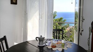 Un tavolo da pranzo con una caffettiera, un piatto con cibo e vista sul mare dal balcone.