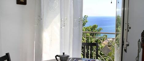 Ett matbord med en kaffekanna, en tallrik med mat och utsikt över havet från en balkong.