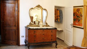 Un comò in legno con specchio e un vaso, una porta e un quadro appeso al muro.