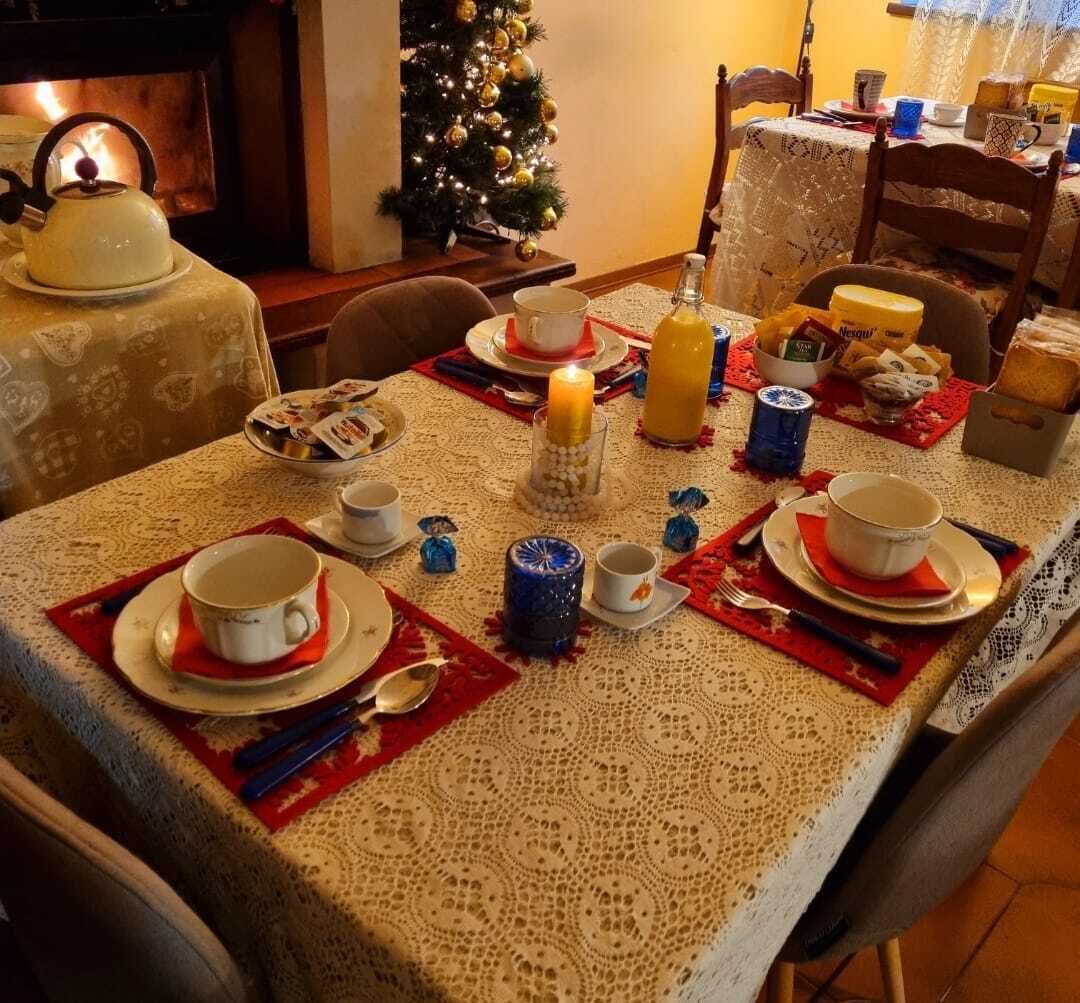 Una mesa de comedor con platos, tazas y una vela, rodeada de sillas y un árbol de Navidad.