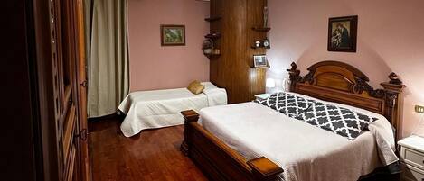 A bedroom with two single beds, a wooden wardrobe, a nightstand, and a ceiling light fixture.