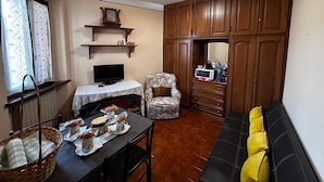 A compact living space with a sofa, a dining table with chairs, a television, wooden cabinets, and a small kitchen area with a microwave and other appliances. - Turquoise fairy family suite (Collodi)