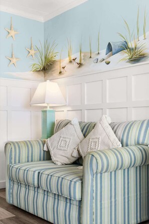 Een gestreept sofa met twee decoratieve kussens, een lamp en een wanddecoratie met zeesterren en planten.