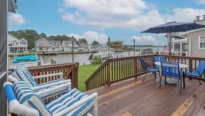 A deck with a view of a marina, a dining table with chairs, and a blue and white striped sofa. - Canalfront Oasis | Boat Dock (Ocean Pines)
