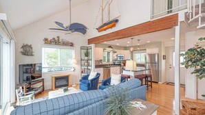 A spacious living room with a large blue sofa, a fireplace, and a kitchen area visible through an open doorway. - Canalfront Oasis | Boat Dock (Ocean Pines)