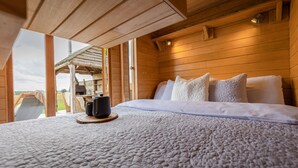 A wooden cabin bedroom with a bed, pillows, and a cup on a coaster. - Tinywood One, dog friendly with hot tub in Warwick (Long Itchington)