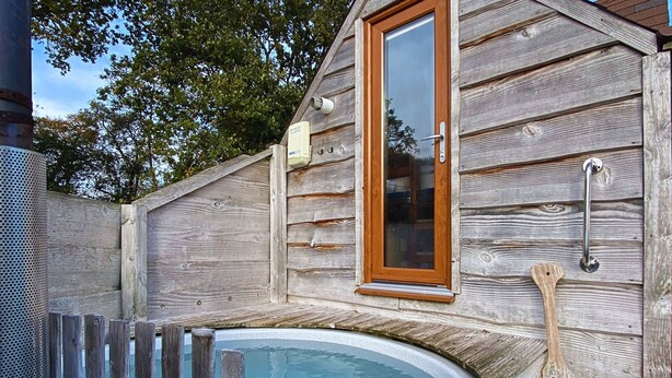 Une cabane en bois avec un bain à remous, une pagaie en bois et une fenêtre qui sert également de porte.