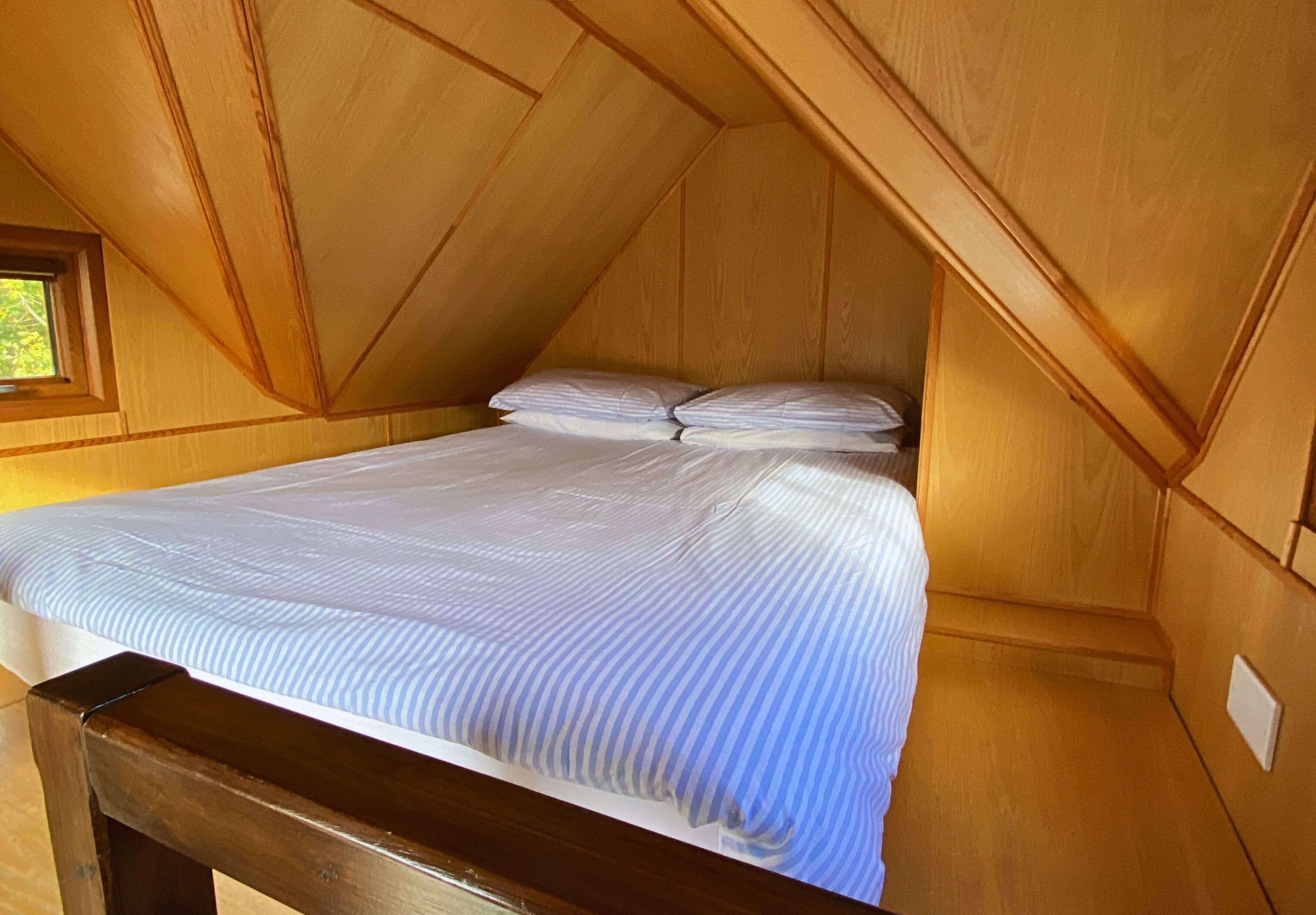 Een zolderkamer met houten lambrisering, een bed, een raam en een houten bankje.