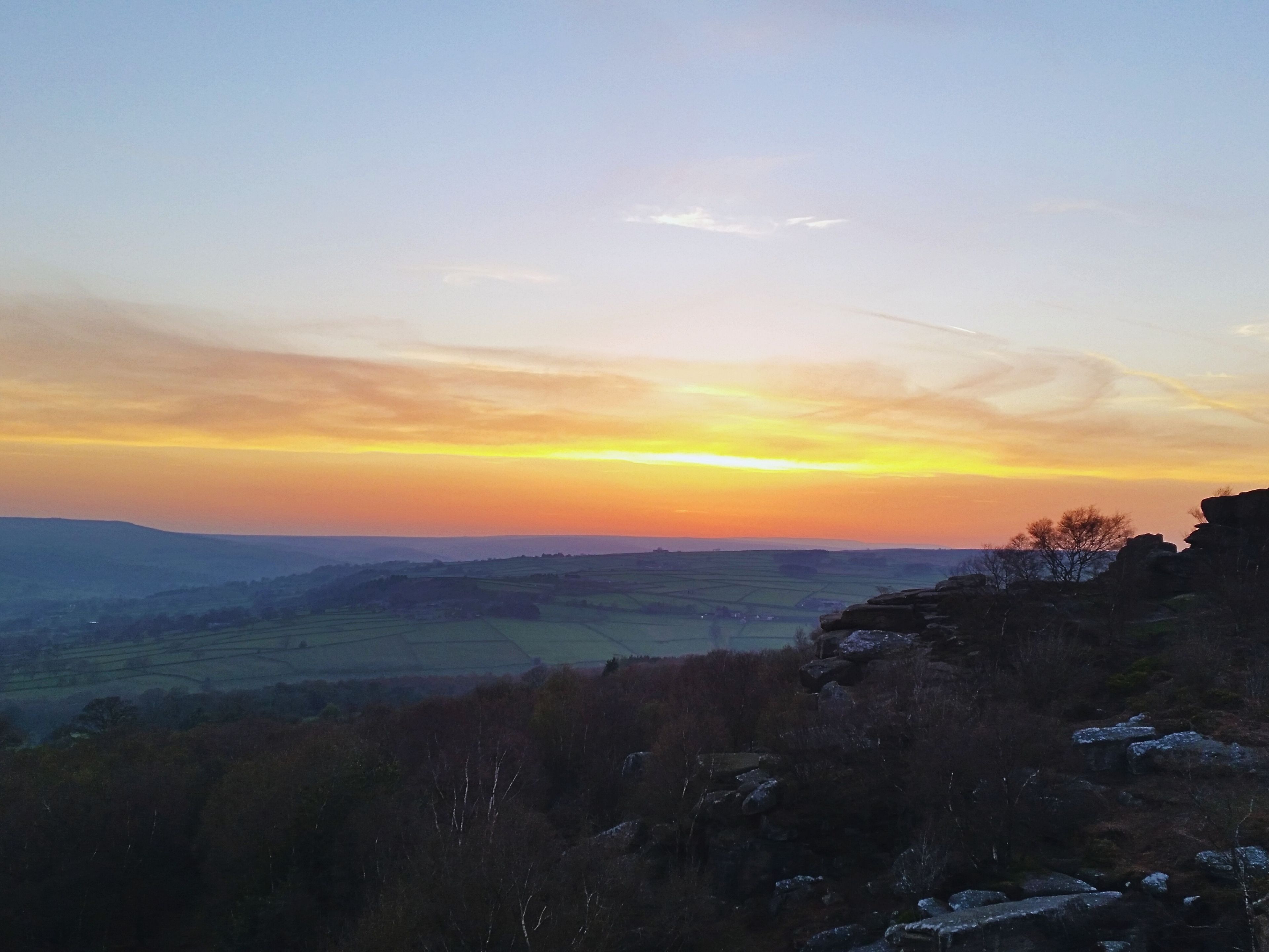 A landscape with a sunset over rolling hills and a rocky outcrop in the foreground.