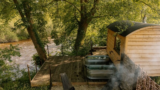 A rustic outdoor cabin with a wooden deck, a metal fire pit, and a hammock. - Dog friendly glamping accommodation in Ripon, Yorkshire (West Tanfield - Ripon)