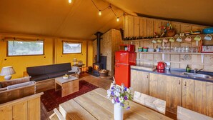 A cozy cabin interior with a wooden dining table, sofa, and kitchen area featuring a red refrigerator and wooden cabinets. - Dog friendly glamping accommodation in Ripon, Yorkshire (West Tanfield - Ripon)