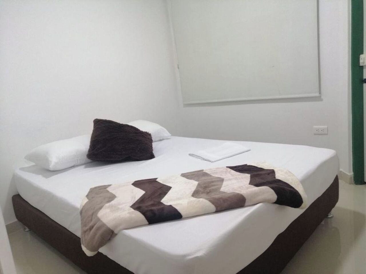 A neatly made bed with a patterned blanket, white pillows, and a dark throw pillow.