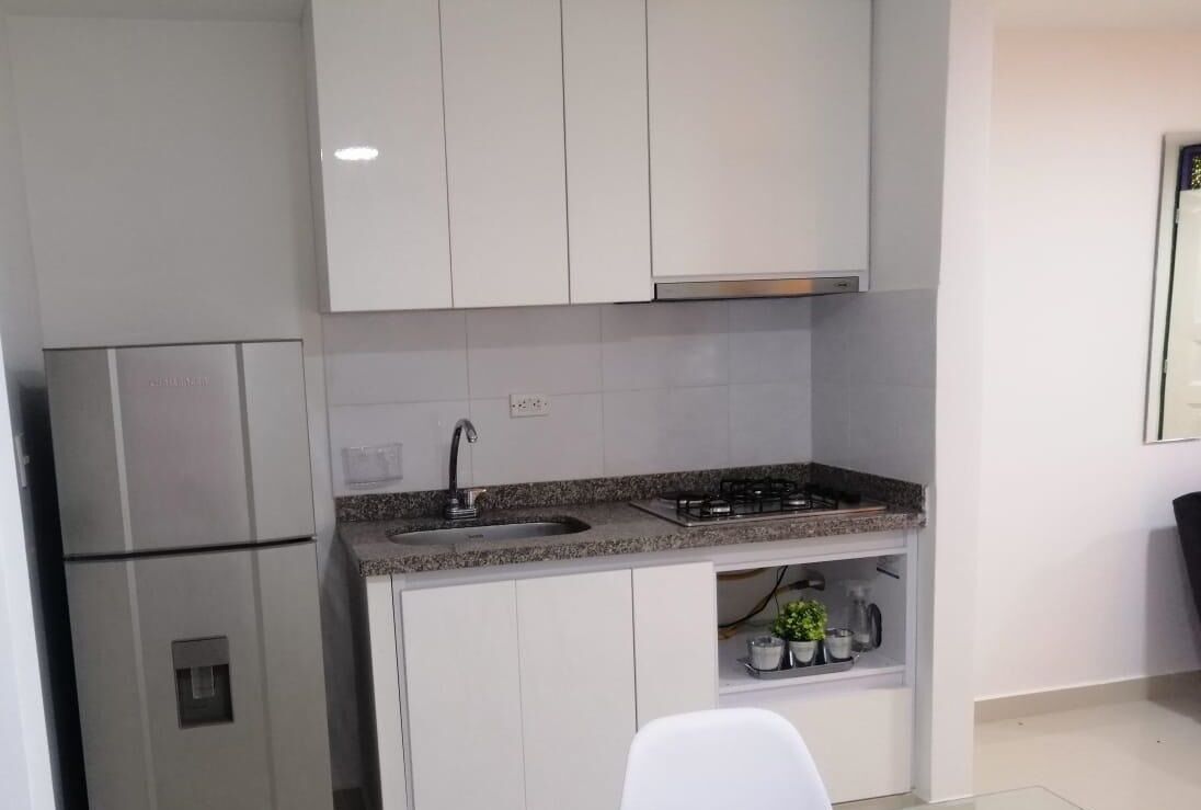 A compact kitchen with white cabinets, a stainless steel refrigerator, a gas stove, and a sink.