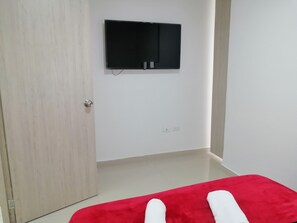 A room with a red bed, a wooden door, a white wall, and a mounted TV. - Near the main park of Salento (Salento)