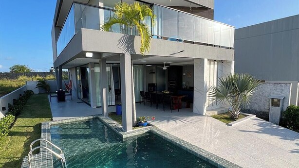 Una casa moderna de dos pisos con piscina, ventanas amplias y un balcón.
