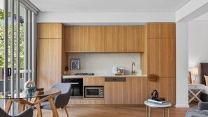 Een moderne keuken met houten kastjes, een eethoek met een glazen tafel en uitzicht op groen.