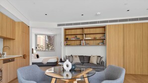 Een moderne woonkamer met een glazen salontafel, grijze fauteuils, een grijze bank en een boekenkast vol boeken.