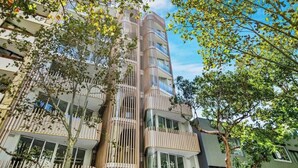 Een meerlaags woongebouw met balkons, omgeven door bomen.