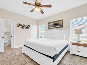 Une chambre à coucher avec un lit, un ventilateur de plafond, un tableau et une table de chevet.