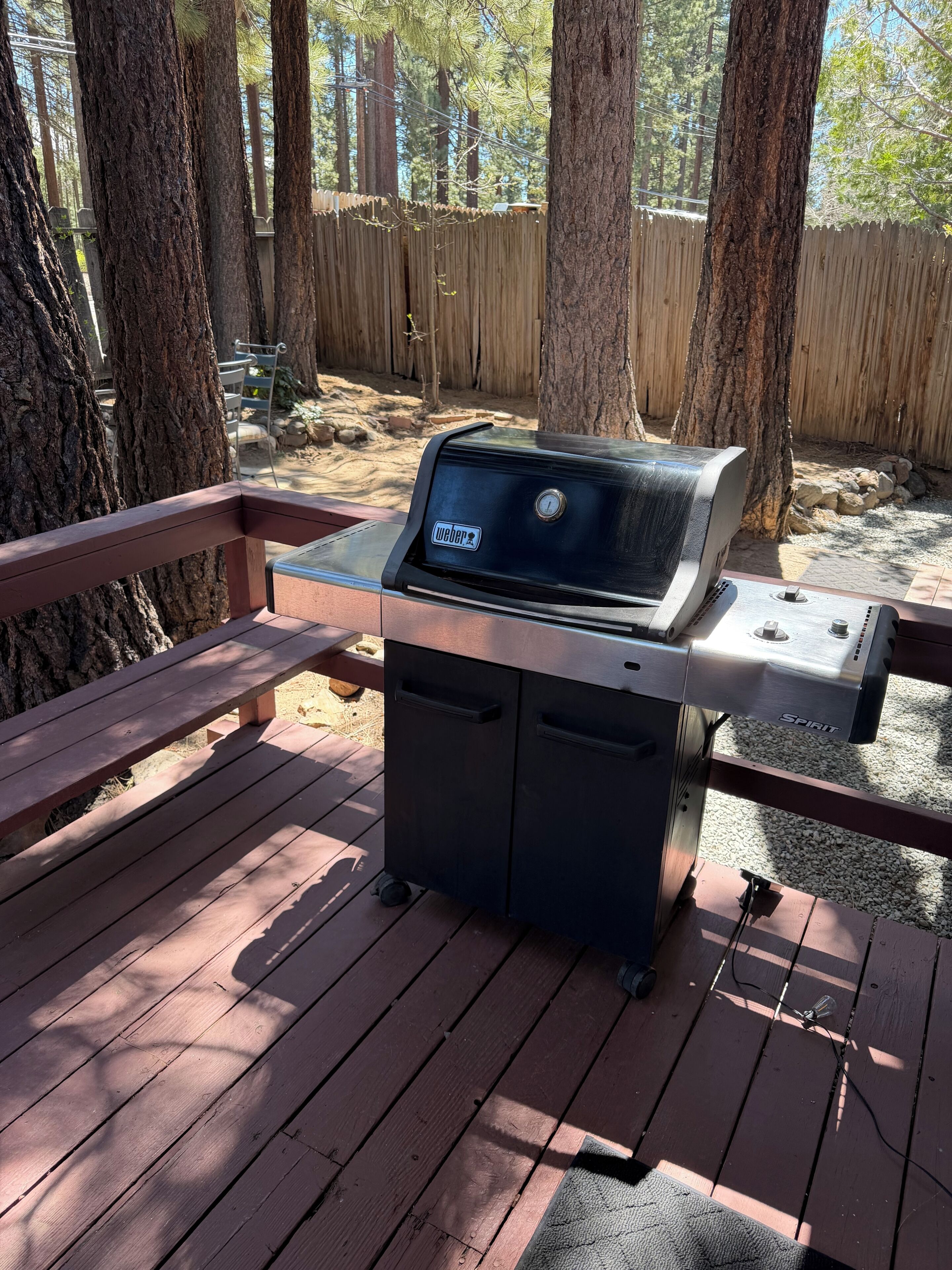 Un barbecue Weber Spirit sur une terrasse en bois, avec une clôture en bois et des arbres en arrière-plan.