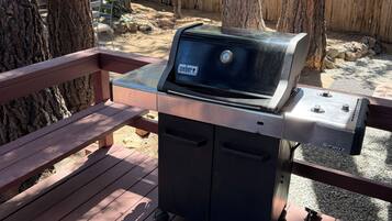 Un barbecue Weber Spirit sur une terrasse en bois, avec une clôture en bois et des arbres en arrière-plan.