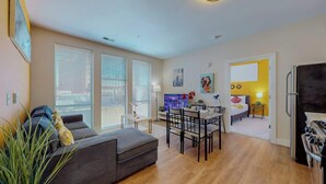A modern apartment with a living room, dining area, and kitchen. There is a large window, a sofa, a dining table with chairs, and a refrigerator. - Stylish Home and Cozy200 (Stamford)