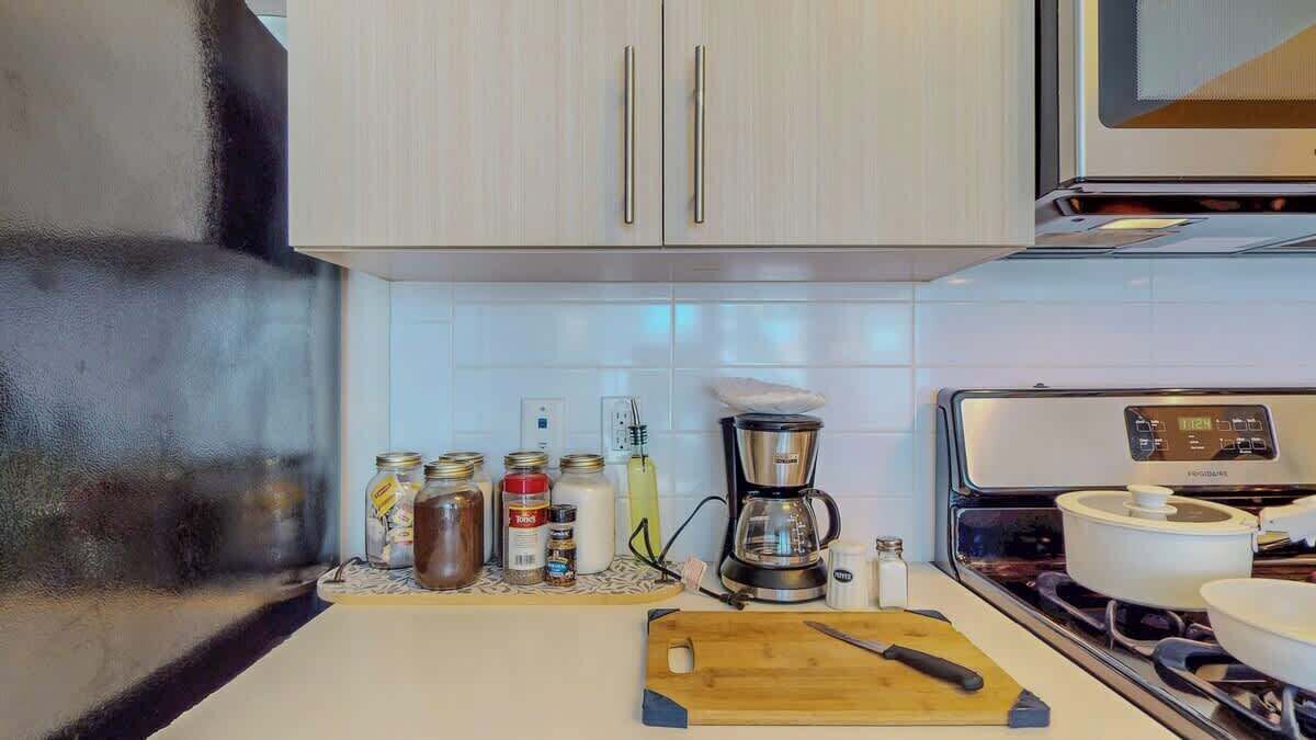 Una cocina con armarios blancos, una cafetera y varios recipientes de comida sobre la encimera.