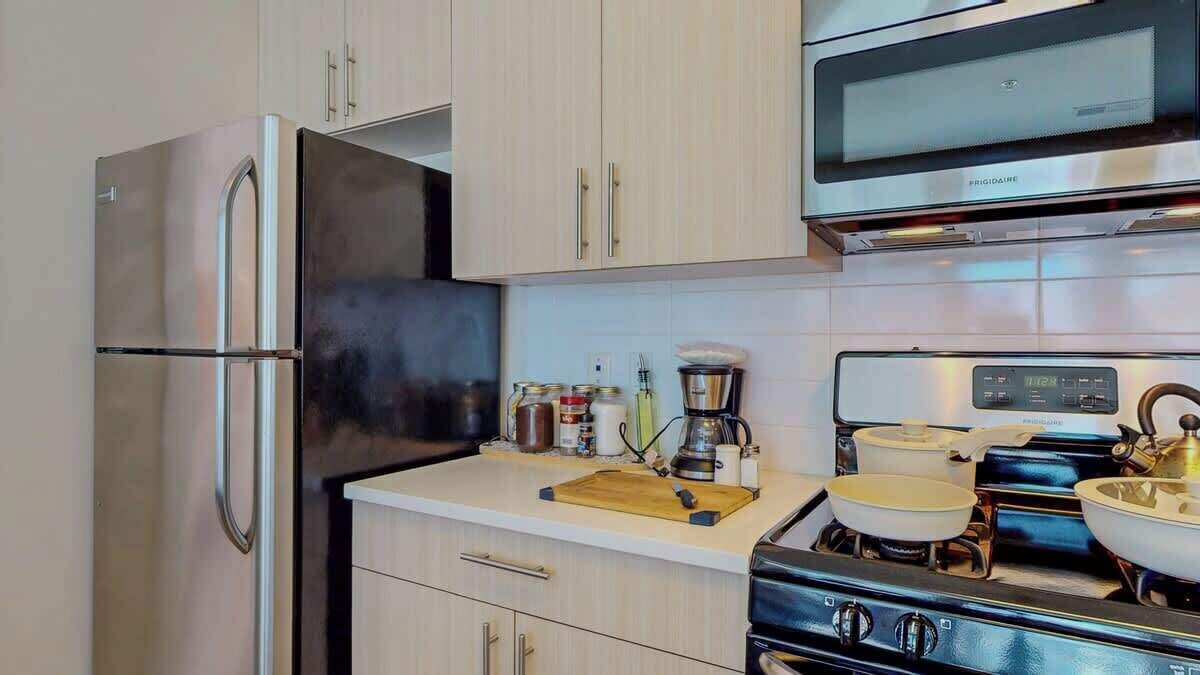 A kitchen with a stainless steel refrigerator, a microwave, a stove, and various kitchen items on the counter.