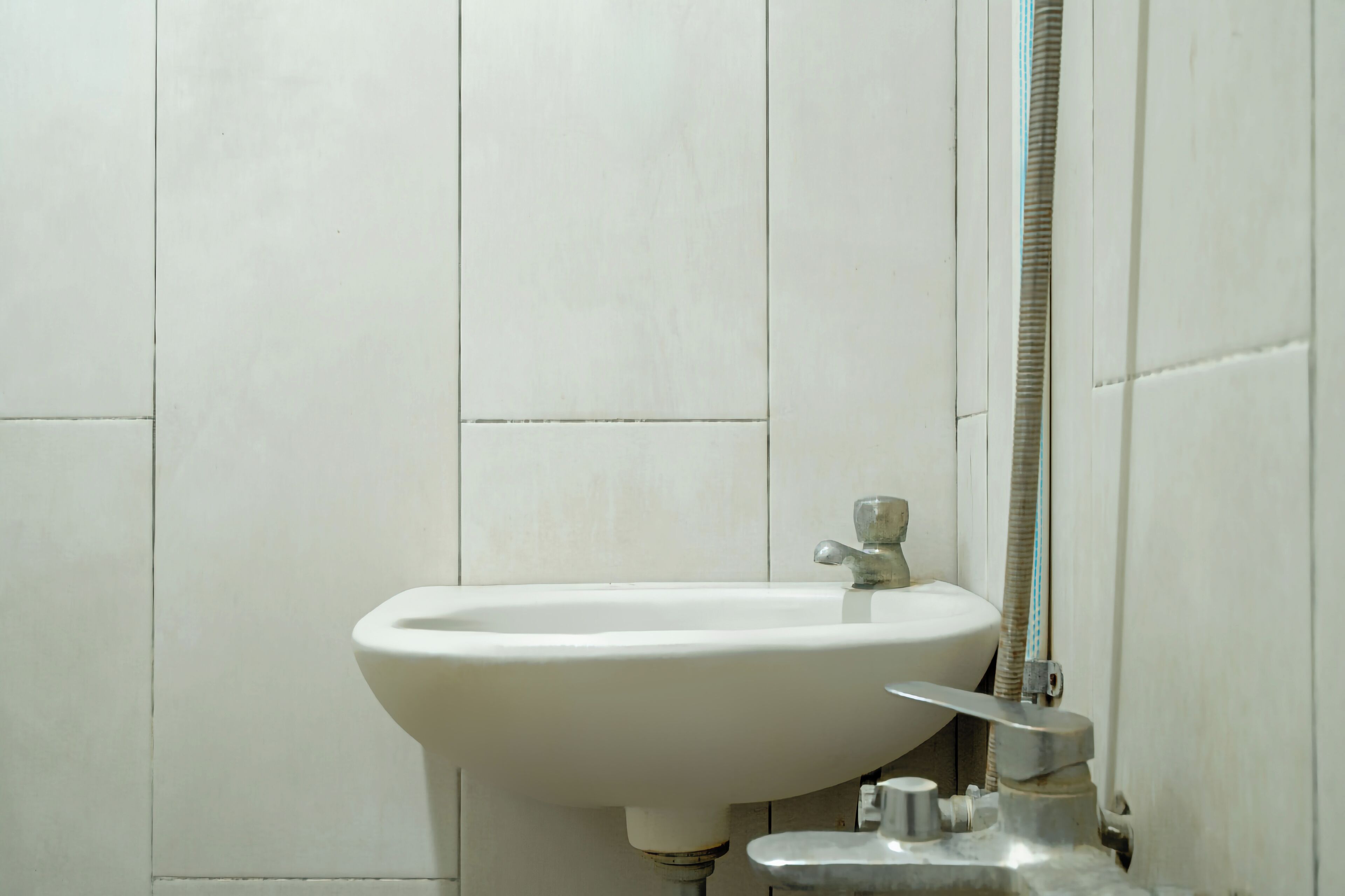A bathroom with a white sink, a faucet, and a shower hose.