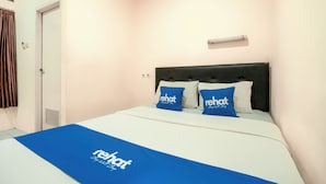 Una habitación de hotel con una cama, dos almohadas con el logotipo del hotel, una colcha azul, una puerta blanca y un interruptor de luz en la pared.