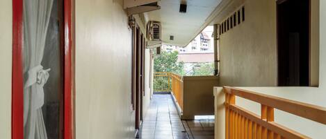 A corridor with a tiled floor, a wooden railing on one side, and a door with a curtain on the other.