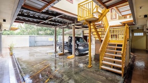 Un área de estacionamiento techada con una camioneta, una escalera y vistas de vegetación al exterior.