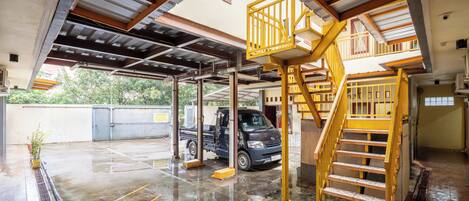 A covered parking area with a truck, a staircase, and a view of greenery outside.