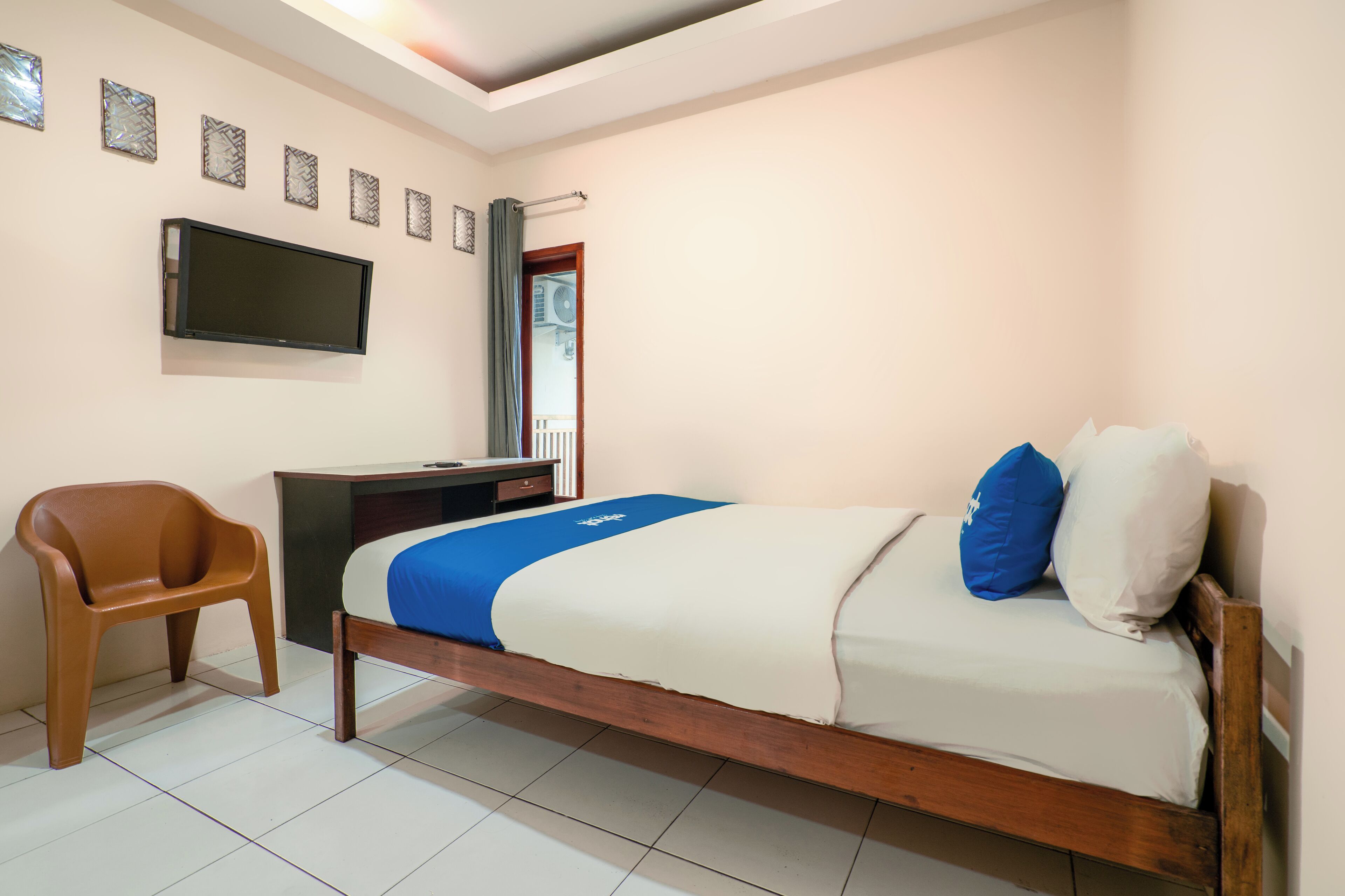 Un dormitorio con cama, escritorio, silla, televisor y ventana con cortinas.