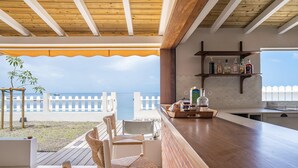 Eine Strandbar mit Korbstühlen, einer Holzbalkendecke und Blick auf das Meer.