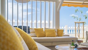 Ein Balkon mit Meerblick, ein Sofa mit gelben Kissen und ein Tisch mit Flaschen und Gläsern.