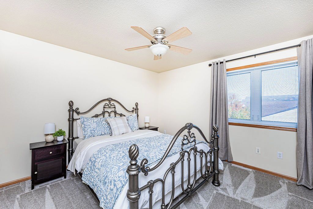 Une chambre à coucher avec un lit, une table de chevet, un ventilateur de plafond et une fenêtre avec des rideaux.