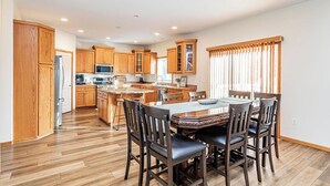 A spacious kitchen with wooden cabinets, a central island, and a dining area with a large table and chairs. - 5BR I Sleeps 10, King x2, Pack n Play, Air Hockey (Fargo)