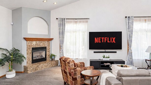A living room with a fireplace, a sofa, a coffee table, and a TV displaying 'NETFLIX'. - 5BR I Sleeps 10, King x2, Pack n Play, Air Hockey (Fargo)