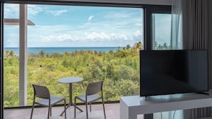 Ein Balkon mit Fernseher, zwei Stühlen und einem Tisch mit Blick auf eine tropische Landschaft und den Ozean.