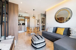 Una sala de estar moderna con un sofá gris, un espejo redondo y un reposapiés estampado.